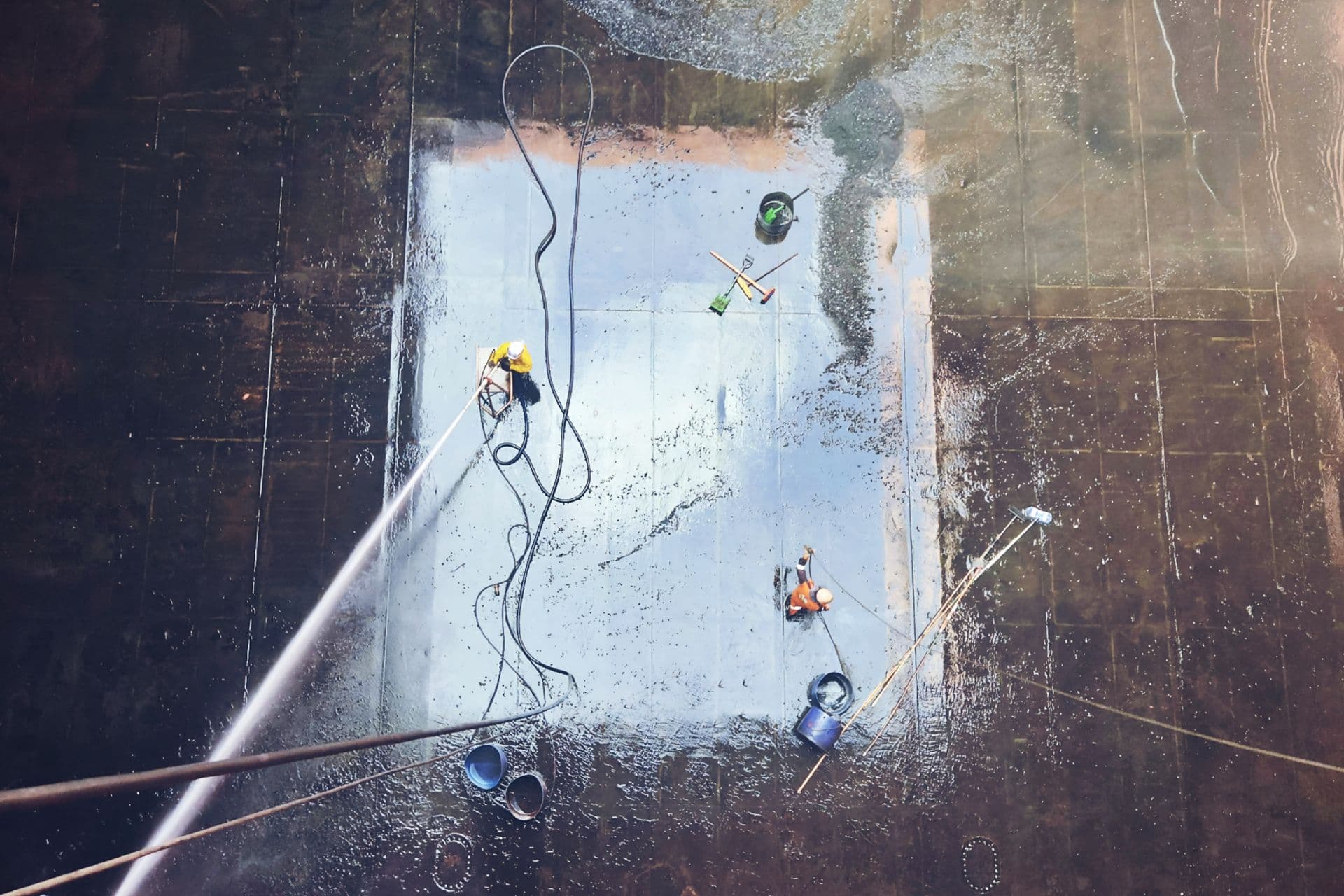 Workers cleaning a large industrial floor surface with hoses and squeegees