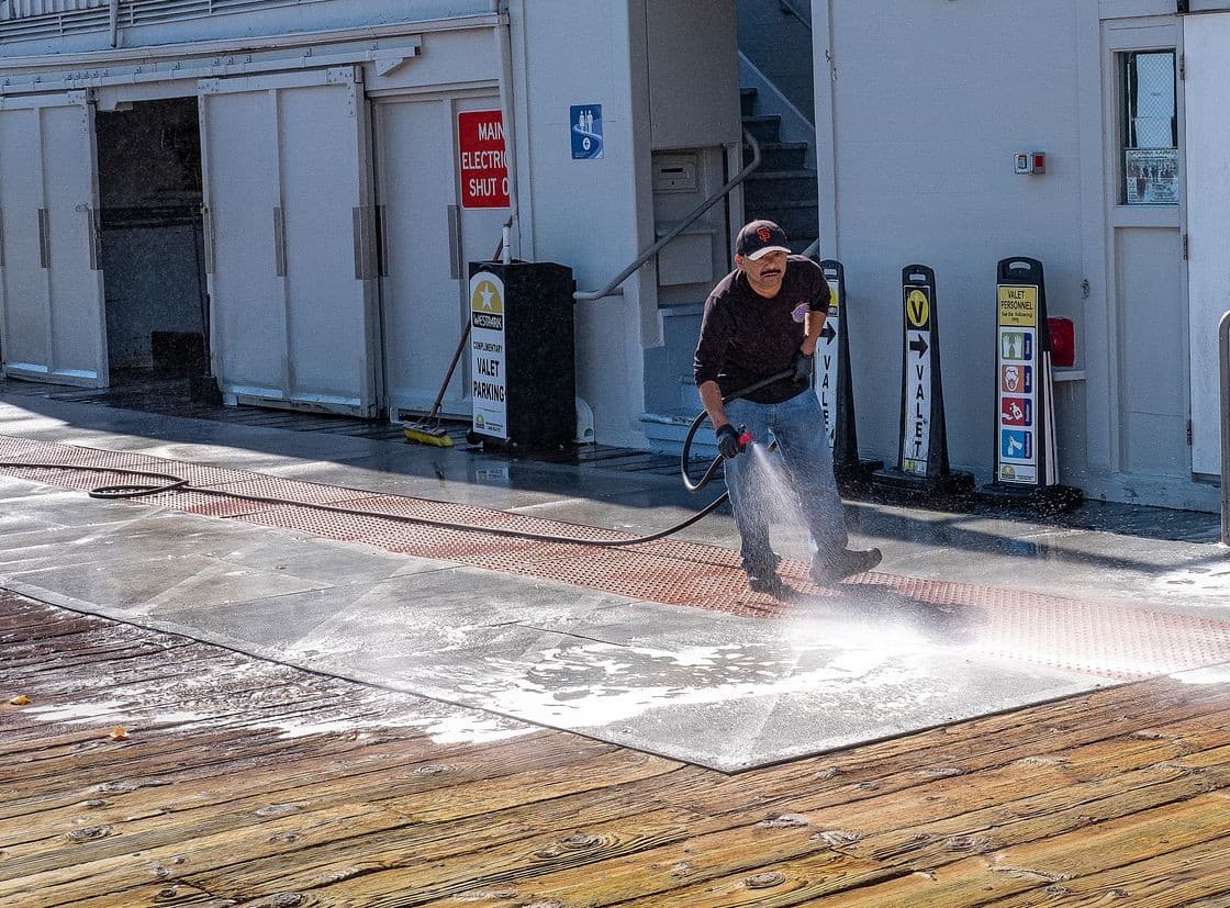 Worker pressure washing a sidewalk outside a commercial building